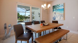 Uma área de refeições com mesa de madeira, seis cadeiras, um banco, um candelabro e uma pintura representando uma cena de praia.