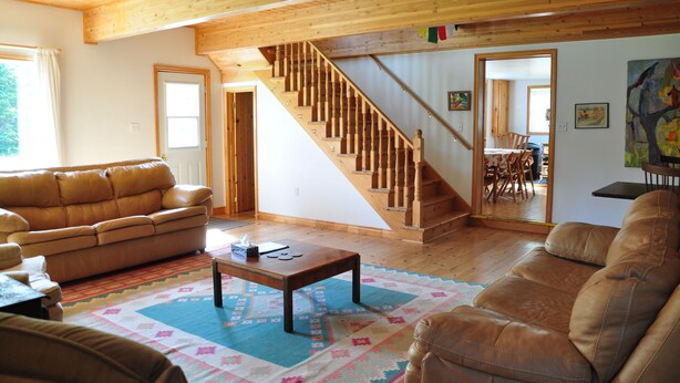 Un salón amplio con una escalera de madera, sofás de cuero y una alfombra colorida.