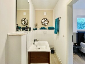 Un baño moderno con un lavabo blanco, un espejo y un perchero para toallas.