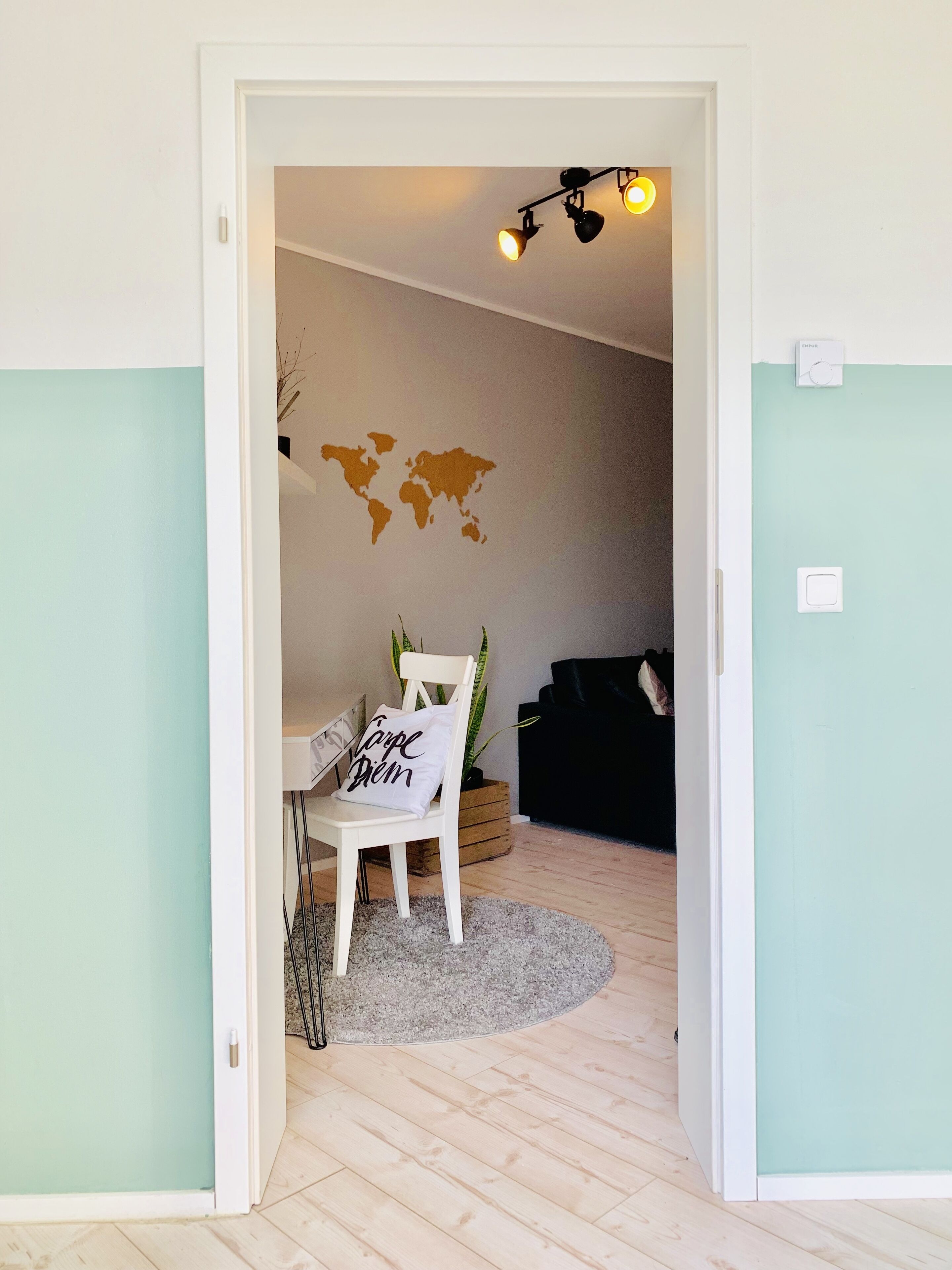 A room with a white chair, a world map on the wall, a black sofa, and a small plant.