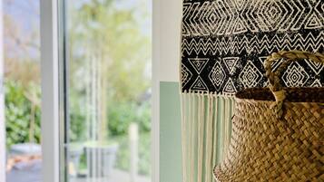 A woven basket with a handle, a patterned fabric, and a view of a green outdoor area through a window.