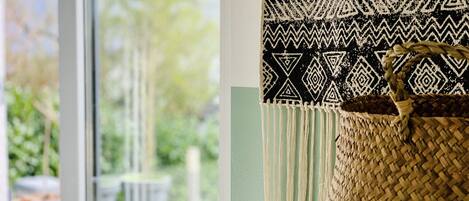 A woven basket with a handle, a patterned fabric, and a view of a green outdoor area through a window.