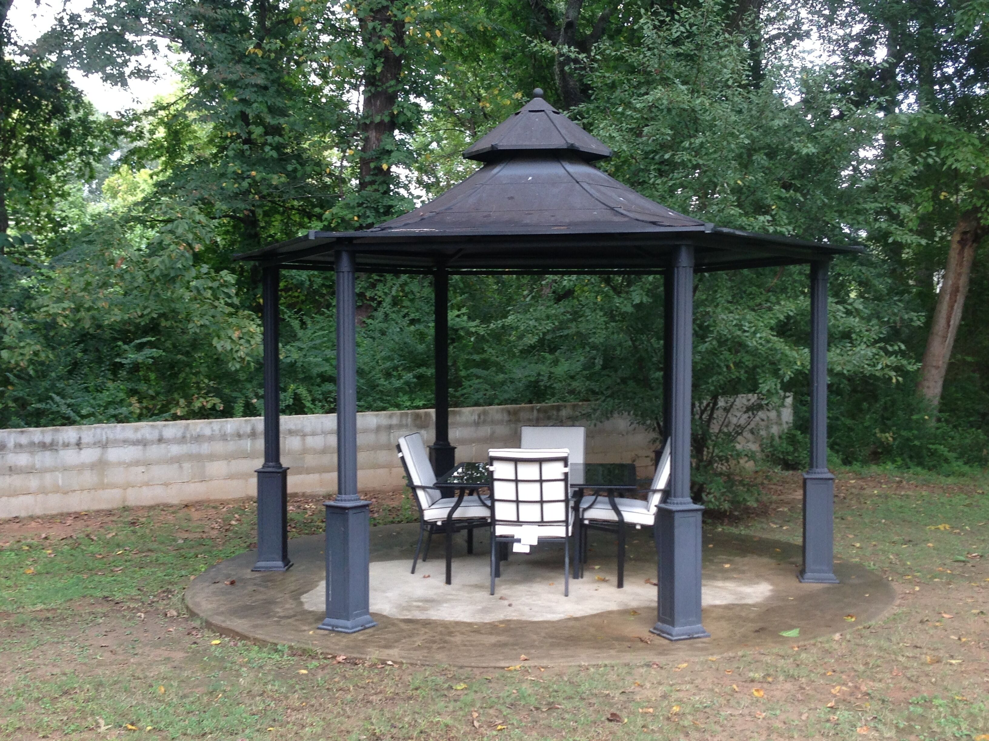 Un kiosque doté d’un toit hexagonal et de quatre chaises.