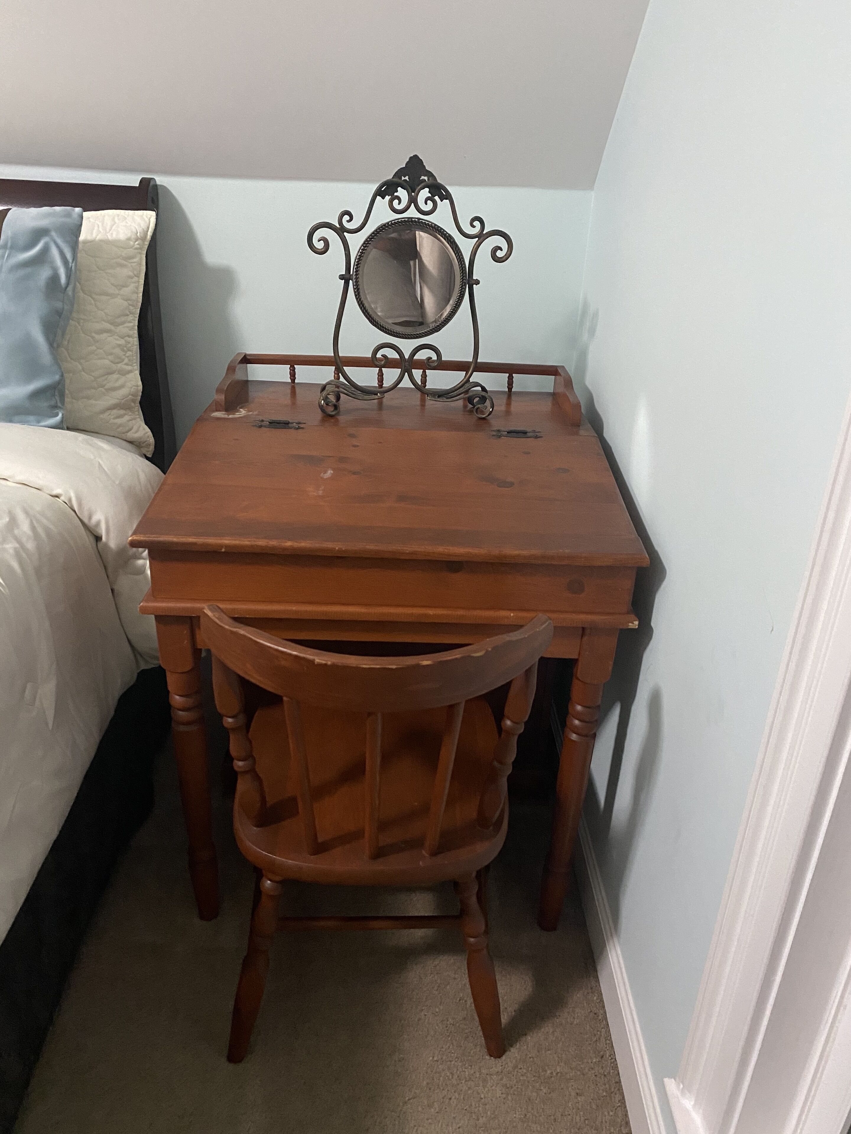 A small wooden table with a mirror and a chair in a room with a bed and light blue walls.