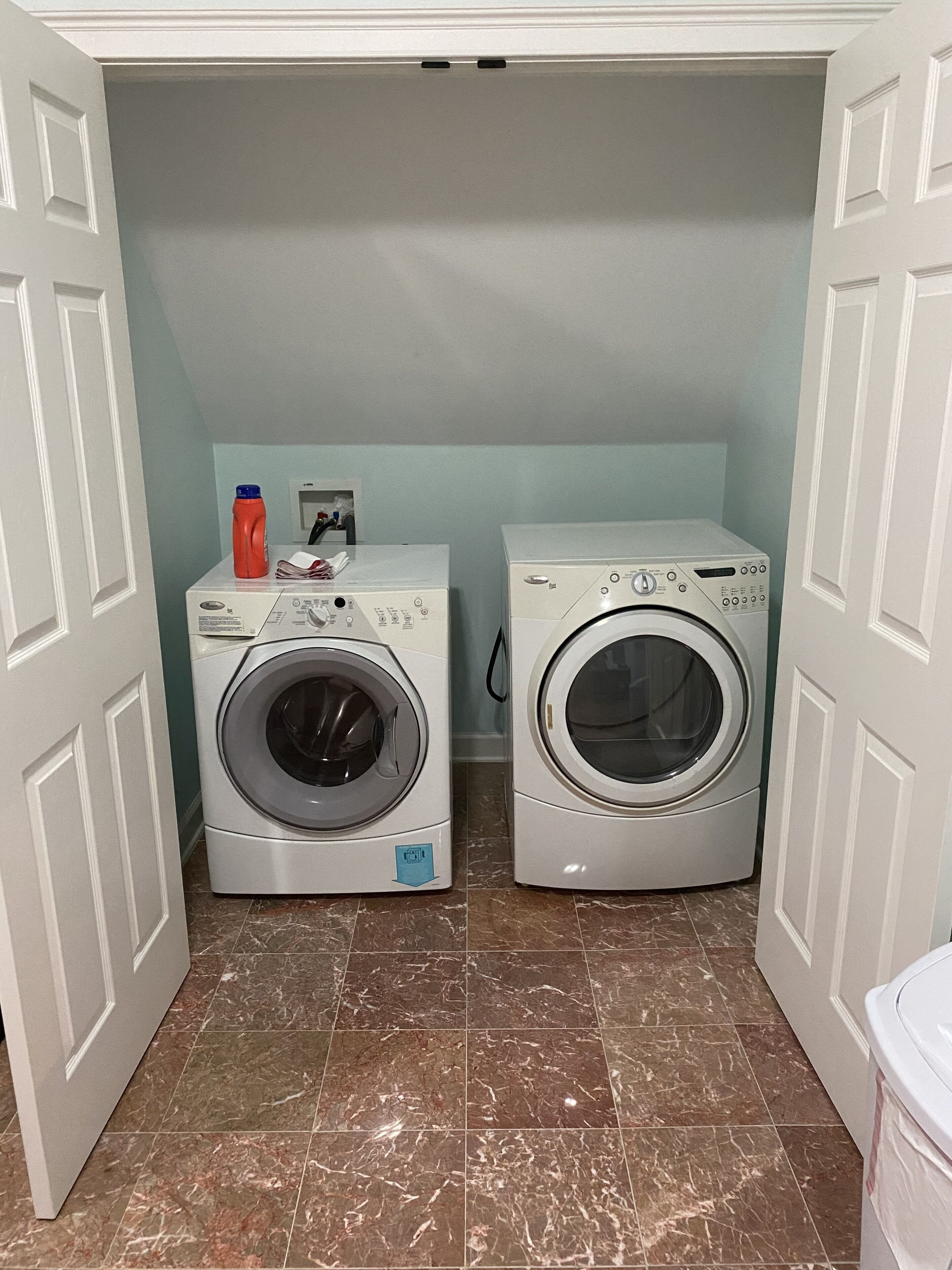 A laundry room with two front-loading washing machines and a red detergent bottle on the left.