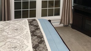 Un dormitorio con un ventanal grande, una cama con ropa de cama estampada y un televisor sobre un mueble.