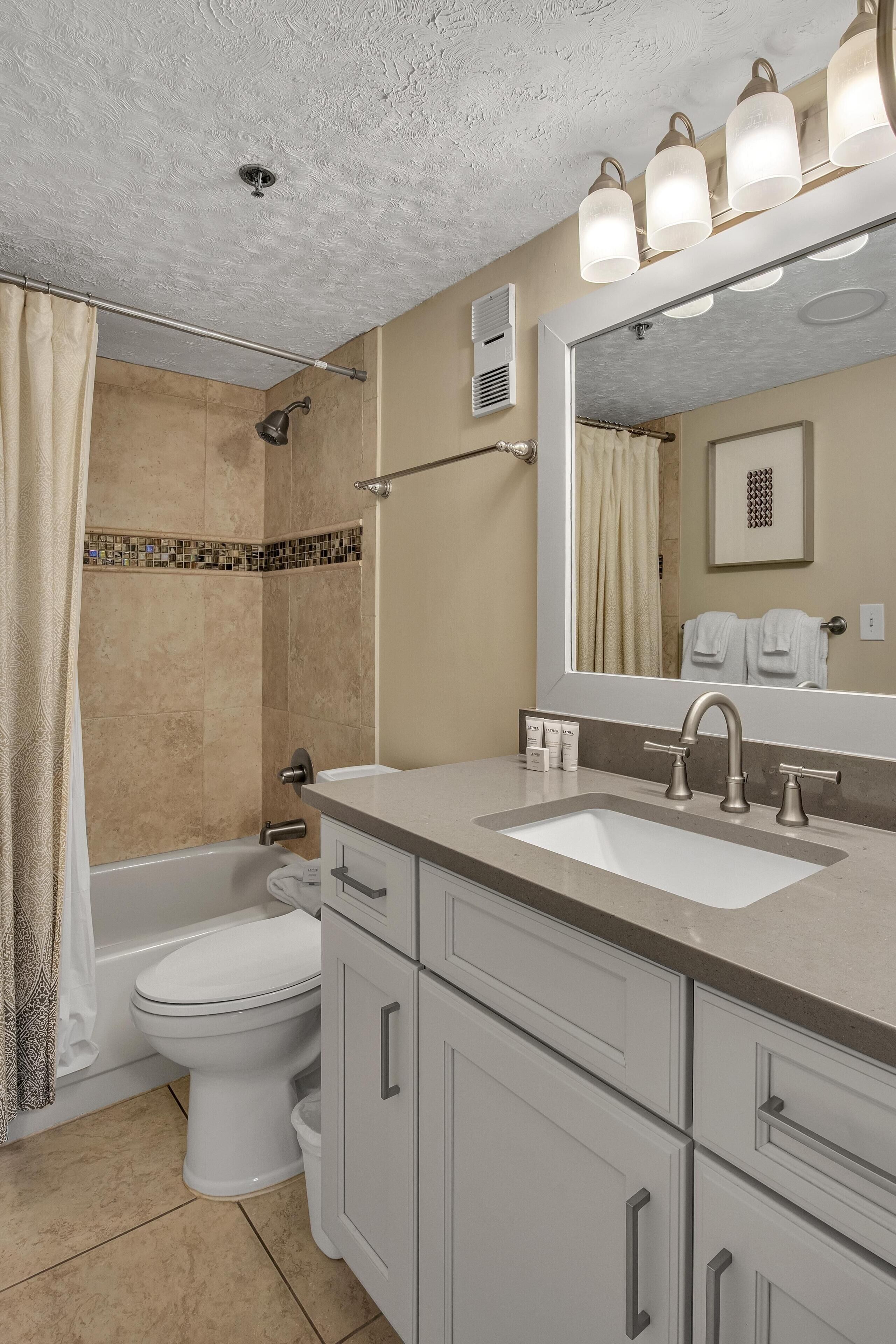 Un baño con bañera, inodoro, tocador con lavabo y un espejo grande.