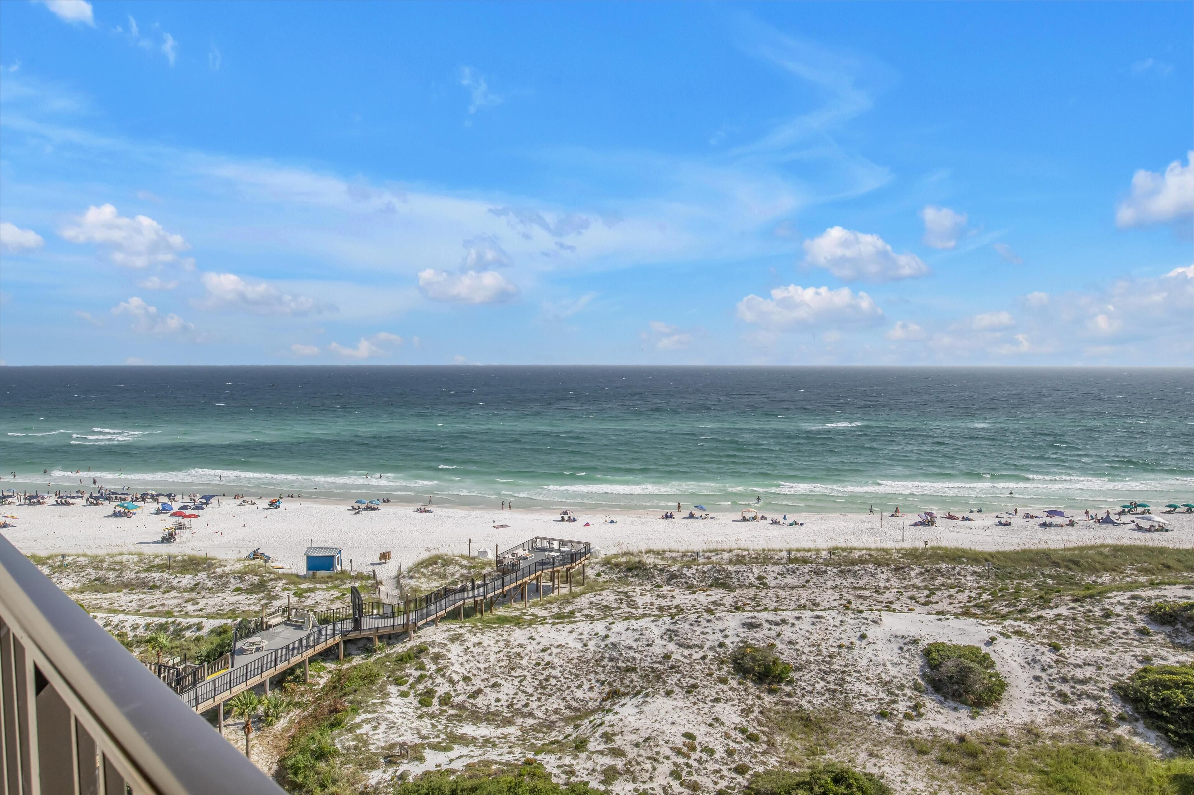 A beach view with a sandy shore, a pier, and a clear sky.