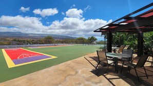Un patio al aire libre con cancha de tenis, asientos y vista a montañas distantes.