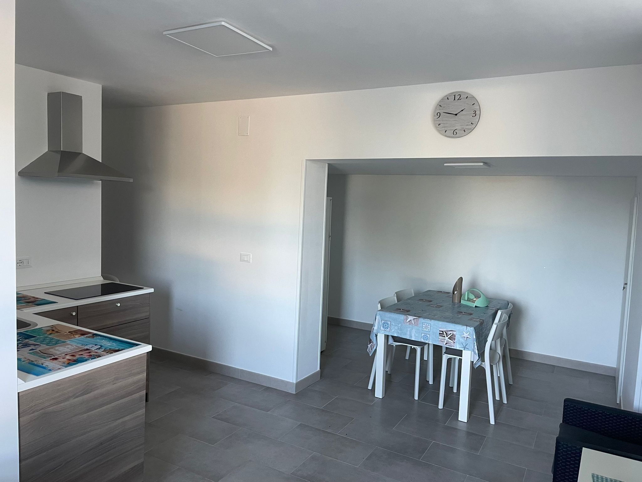 Une cuisine moderne équipée d’une cuisinière intégrée, un coin repas avec une table et des chaises, et une horloge au mur.