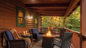 Een houten chalet met een overdekte veranda, rieten meubilair, een vuurkuil en uitzicht op herfstkleuren.