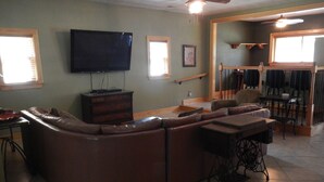 Una sala de estar con un sofá modular grande en forma de L, un televisor de pantalla plana montado en la pared y una zona de comedor con una mesa y sillas de madera.