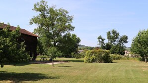 Un área con césped, una mesa de picnic, un edificio de madera y árboles.