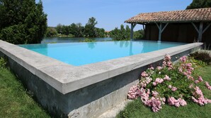 Una piscina con borde de hormigón, rodeada de césped y flores rosadas.