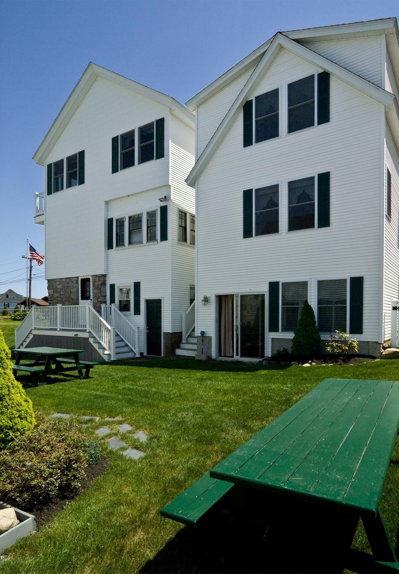 A two-story white building with a covered patio and a picnic table.