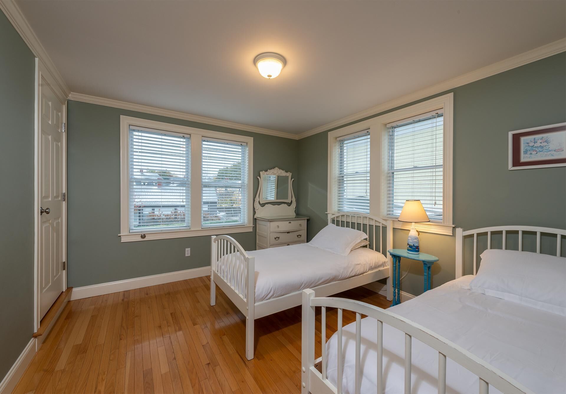 A bedroom with two single beds, a dresser, a nightstand, a lamp, and a window with blinds.