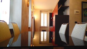 Corredor de hotel com piso de madeira, porta com painéis de vidro jateado e espelho refletindo o ambiente.