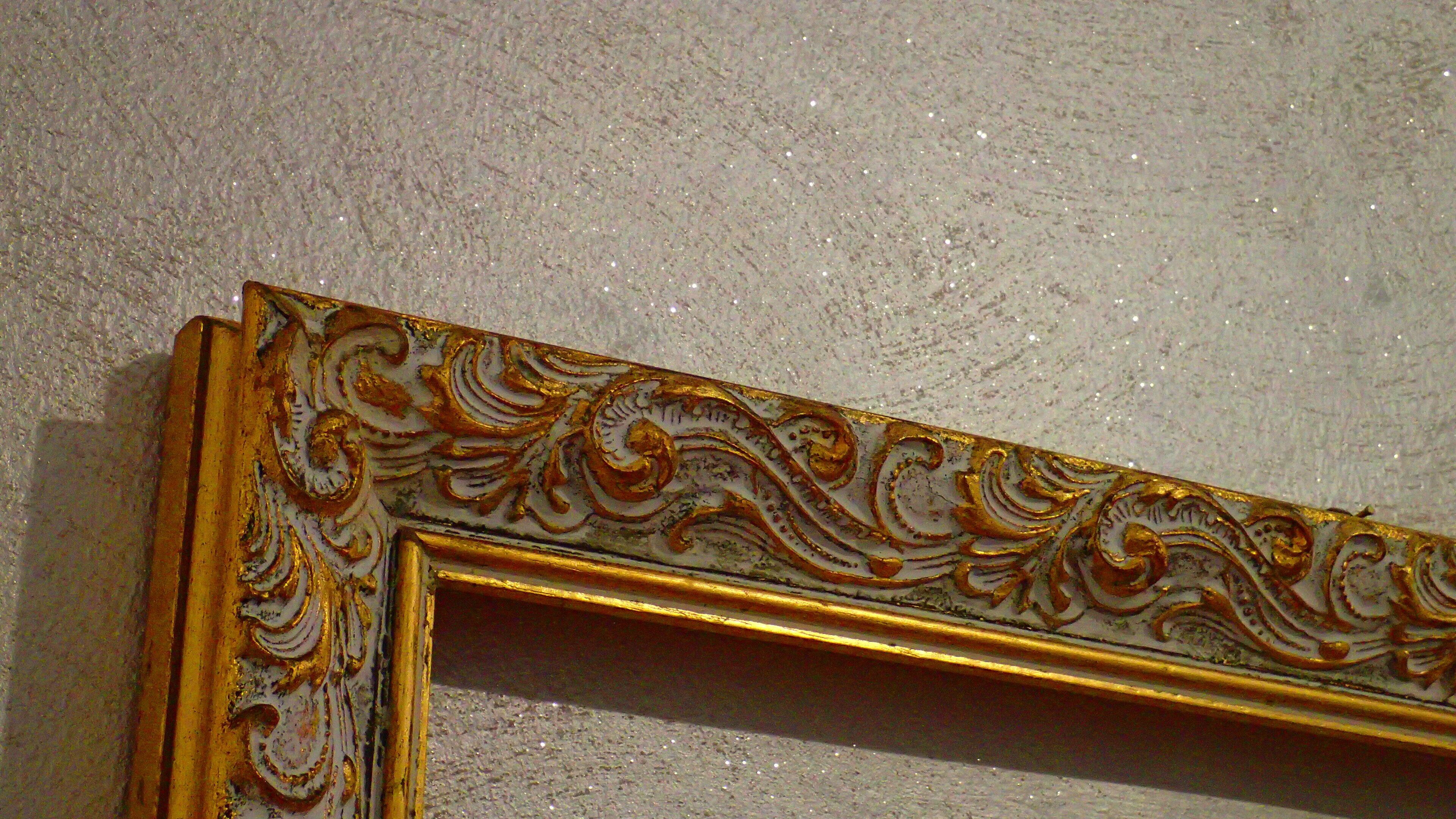 Un espejo con marco dorado y detalles decorativos sobre una pared con textura.