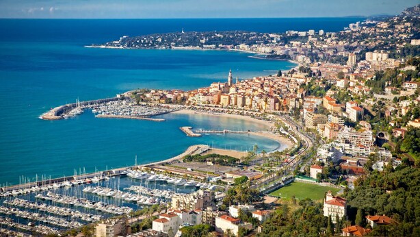 Paisagem costeira com um porto de recreio, edifícios e um céu azul límpido.