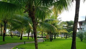 A well-maintained garden with palm trees and a paved walkway. - PORTO DE GALINHAS BANGALO PREMIUM AT THE BEACH CLASS HOTEL (ipojuca)