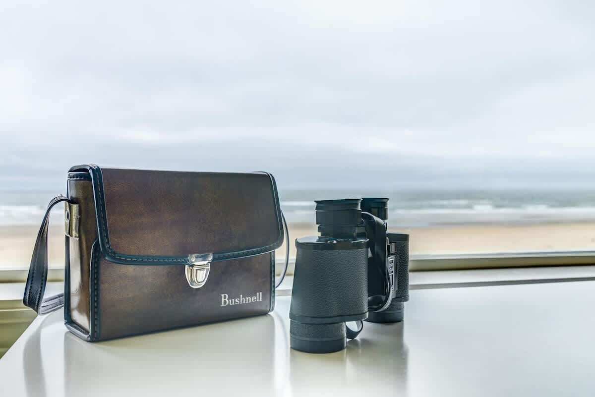 A leather bag and binoculars on a table with a view of the beach.