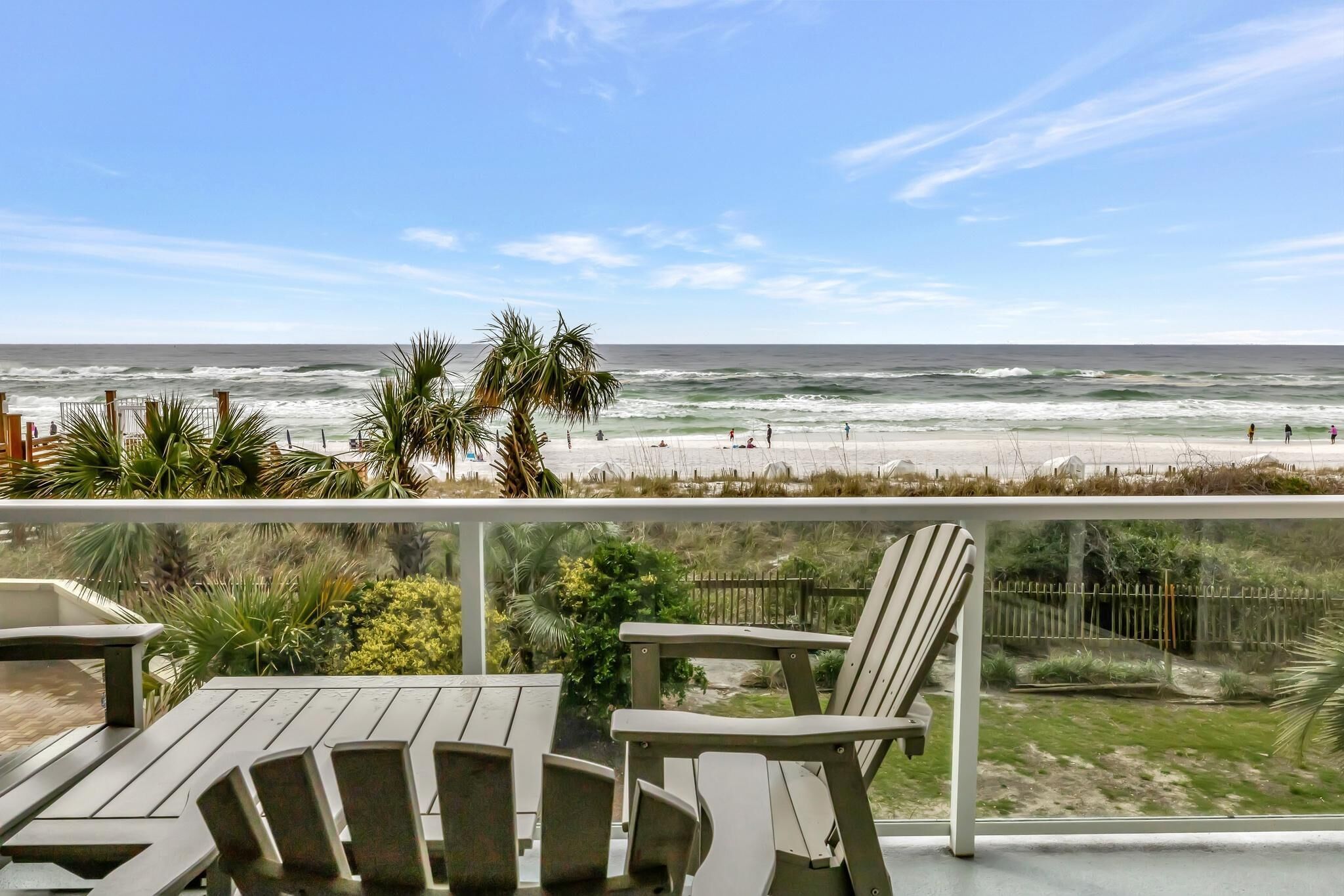A beach view from a balcony with chairs and a railing.