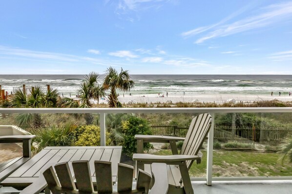 A beach view from a balcony with chairs and a railing.