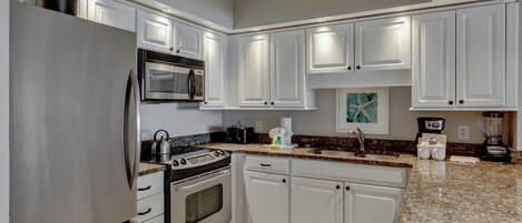 A modern kitchen with white cabinetry, stainless steel appliances, granite countertops, and a built-in microwave.