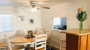 A dining area with a round wooden table, white chairs, a ceiling fan, and a small decorative plant on a wooden counter.