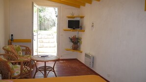 A room with wicker chairs, a small round table, a bed with a striped bedspread, a TV on a shelf, and a door leading outside. - Small studio with all mod cons and a large shared pool (Lorgues)