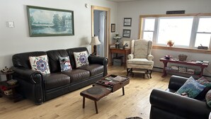Een woonkamer met een zwarte leren bank, een houten salontafel, een witte fauteuil en een boekenplank.