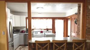 A kitchen with white cabinets, a stainless steel refrigerator, a microwave, and a stove. There is a wooden dining table with four chairs. - Elderberry- Salt Hot Tub, Wood Fireplace, 100+mbps Wifi, Walkable to Downtown (Bend)