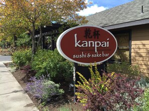 Letrero de un bar de sushi y sake llamado 'kanpai', con un jardín delantero.