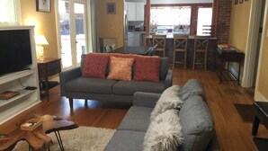 A living room with a grey sofa, a television, and a fluffy dog. - Elderberry- Salt Hot Tub, Wood Fireplace, 100+mbps Wifi, Walkable to Downtown (Bend)