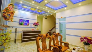 A reception area with a modern ceiling design, a reception desk, a staircase, and traditional wooden chairs.