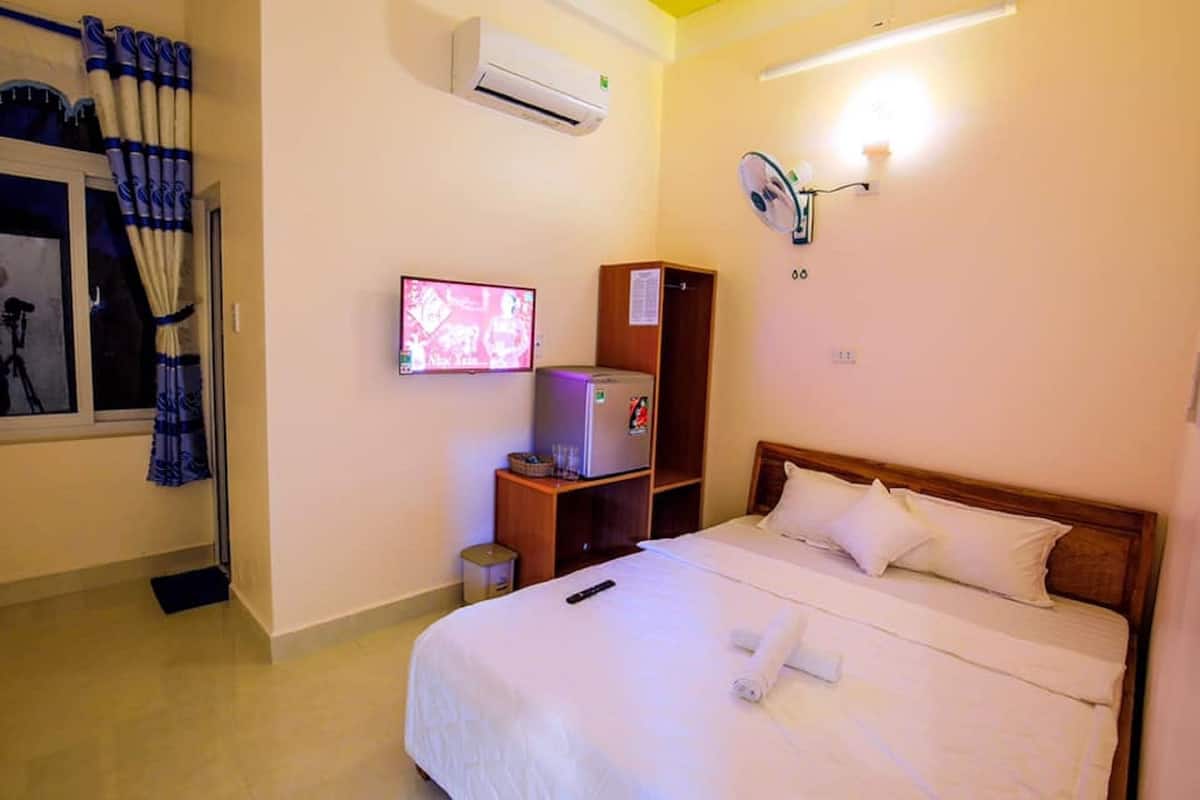 Une chambre d’hôtel équipée d’un lit, d’une télévision, d’un réfrigérateur et d’une fenêtre avec des rideaux.