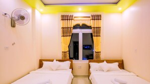 A hotel room with two single beds, a wall-mounted fan, and a window with curtains.