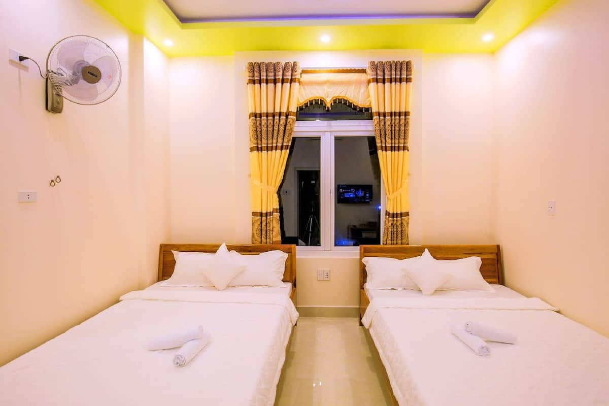 Une chambre d’hôtel avec deux lits simples, un ventilateur fixé au mur et une fenêtre avec des rideaux.