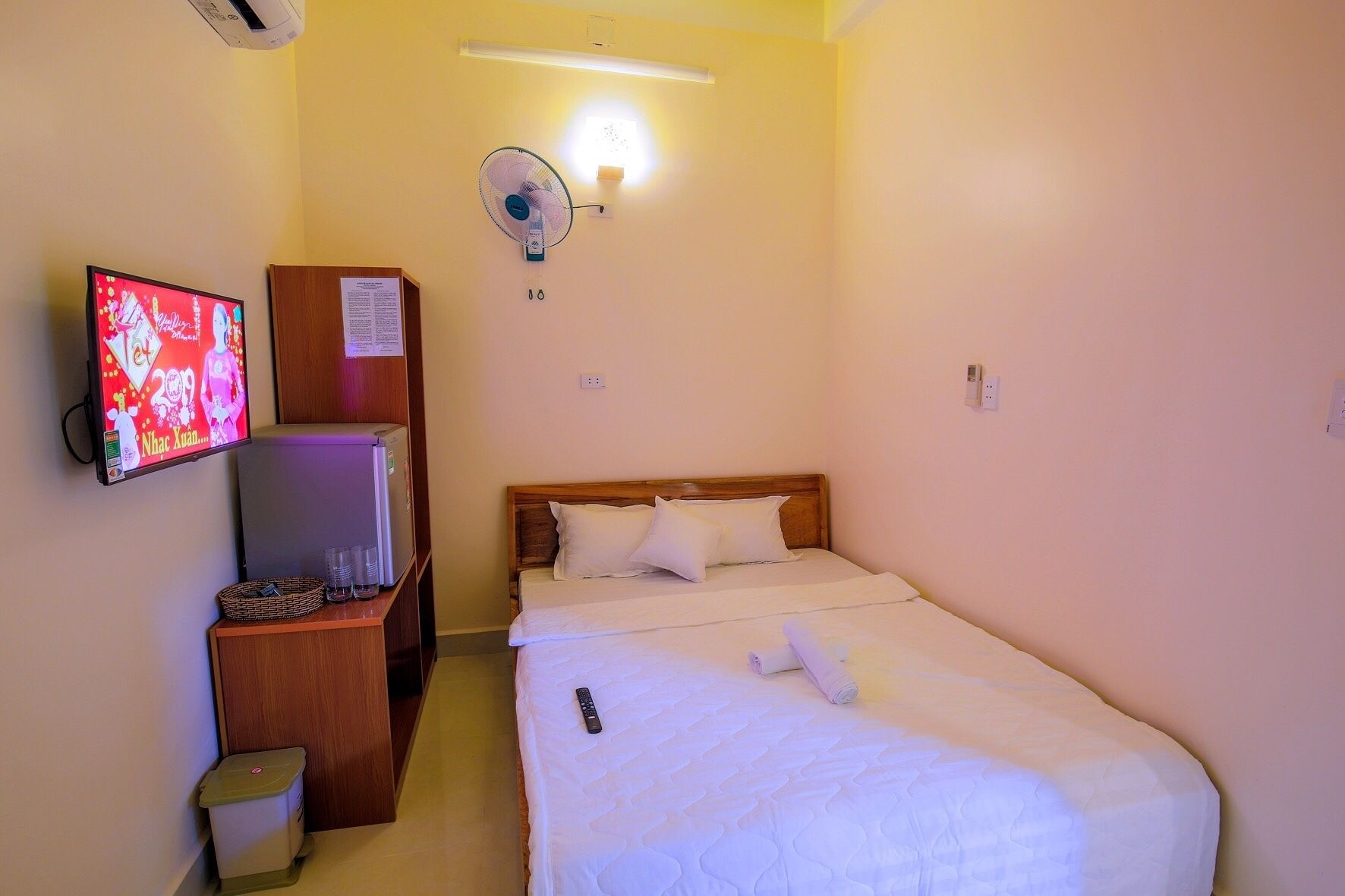 Une chambre d’hôtel équipée d’un lit, d’une télévision, d’un réfrigérateur, d’un ventilateur et d’une poubelle.