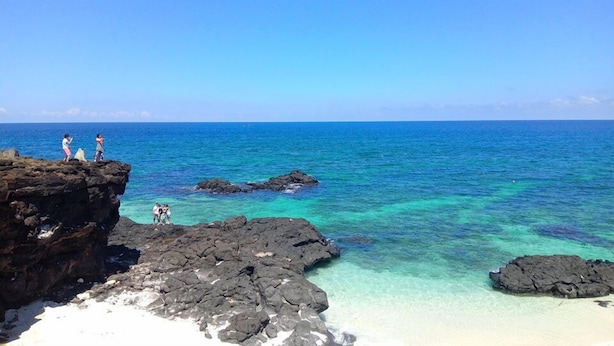 A rocky coastline with clear turquoise waters and a sandy beach.
