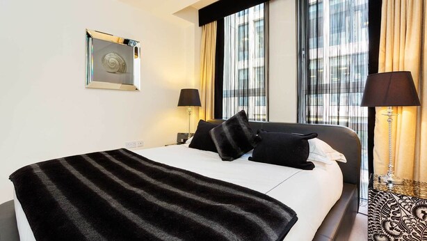 Ein Hotelzimmer mit einem großen Bett, zwei Nachttischlampen, einem fensterbelaubten Fenster und einem Wandkunstwerk.