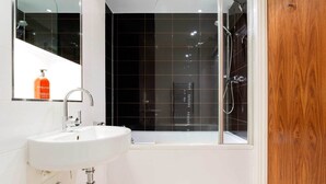 Ein modernes Badezimmer mit einem weißen Waschbecken, einer Duschkabine und einer Holztür.