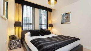 Ein modernes Hotelzimmer mit einem großen Bett, zwei Nachttischlampen, einem dekorativen Spiegel und einem Fenster mit Vorhängen.