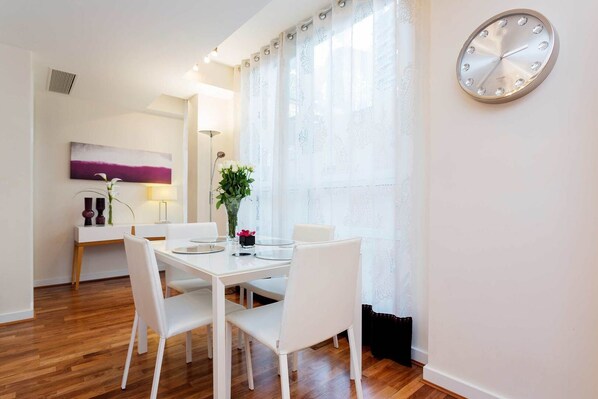 A dining area with a white table, four chairs, a vase with flowers, and a clock on the wall. - Brilliant Barbican, by Veeve (London)