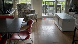 Ein Wohnzimmer mit einer Couch, einem Esstisch mit Stühlen, einem Fernseher und einem Balkon mit Gartenmöbeln.