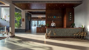 A modern reception area with a wooden reception desk, a receptionist, and a large window providing natural light. - Niraamaya Retreats Samroha Athirappilly (Chalakudy)