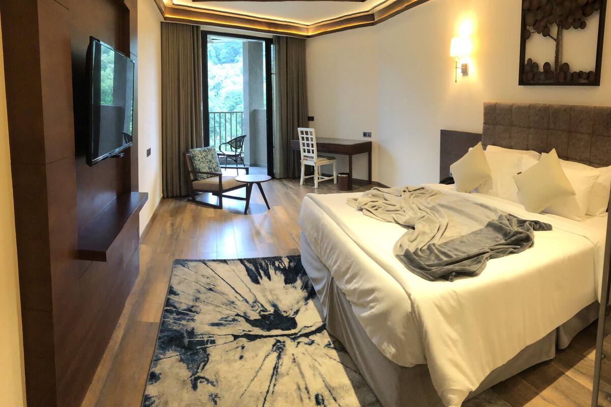 A hotel room with a bed, a desk, a chair, a TV, and a window with curtains.
