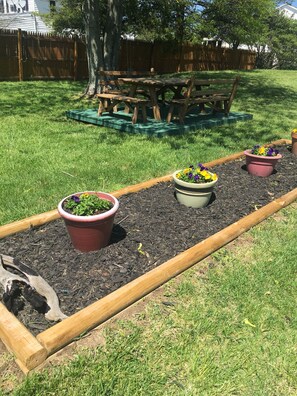A garden with raised beds, wooden benches, and potted plants.