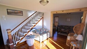 A spacious living room with a wooden staircase, a floral sofa, and wicker chairs. - BEAUTIFUL PEACEFUL, SCENIC, ENJOY CRABS N FISH MEMORABLE, FREE TOUR OF AREA! (Fishing Creek)