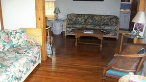 A living room with a floral sofa, a wooden coffee table, a wicker chair, and a small round table with a lamp. - BEAUTIFUL PEACEFUL, SCENIC, ENJOY CRABS N FISH MEMORABLE, FREE TOUR OF AREA! (Fishing Creek)